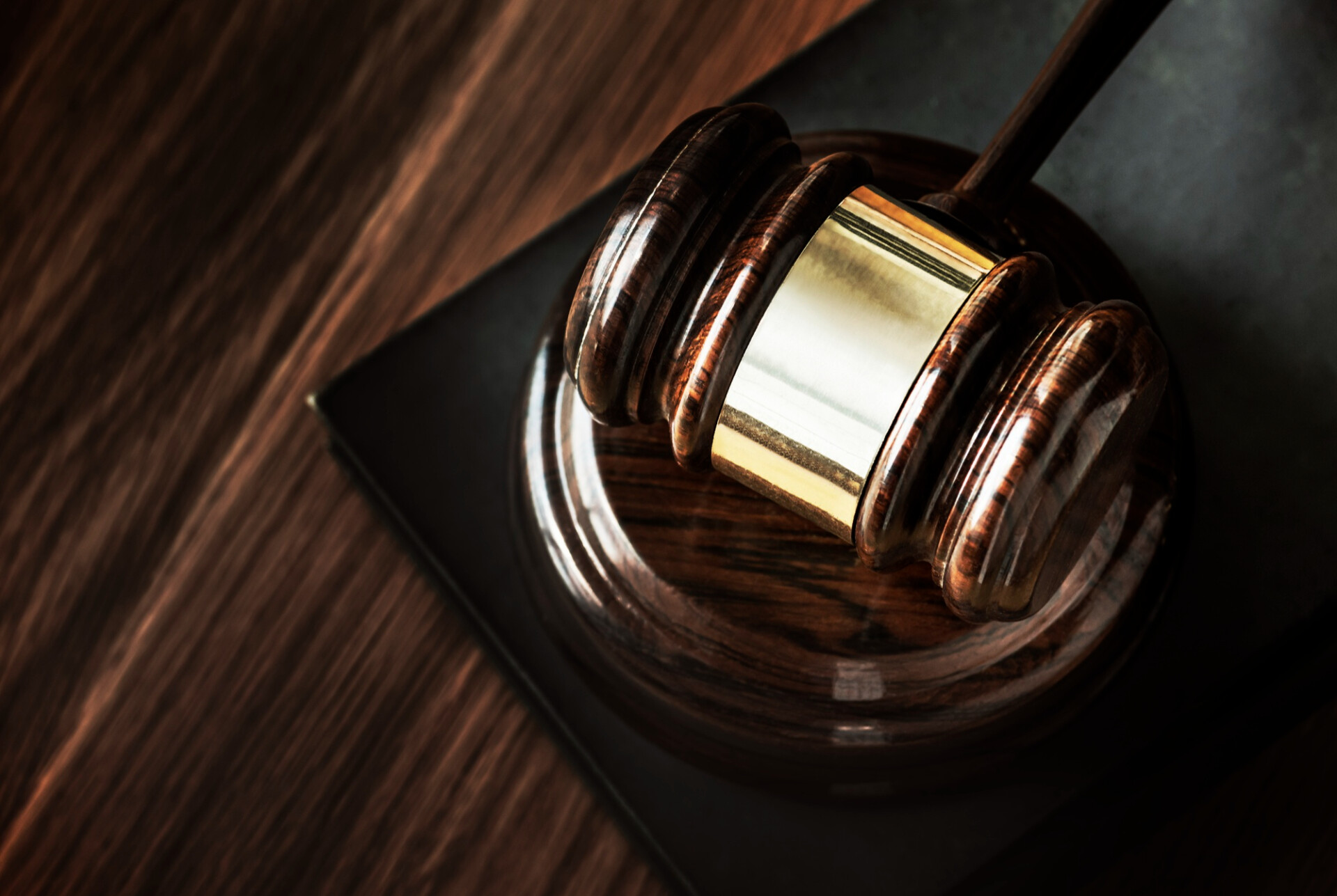 Close-up of a polished wooden judge's gavel resting on a sound block on a dark wood surface, symbolizing justice.