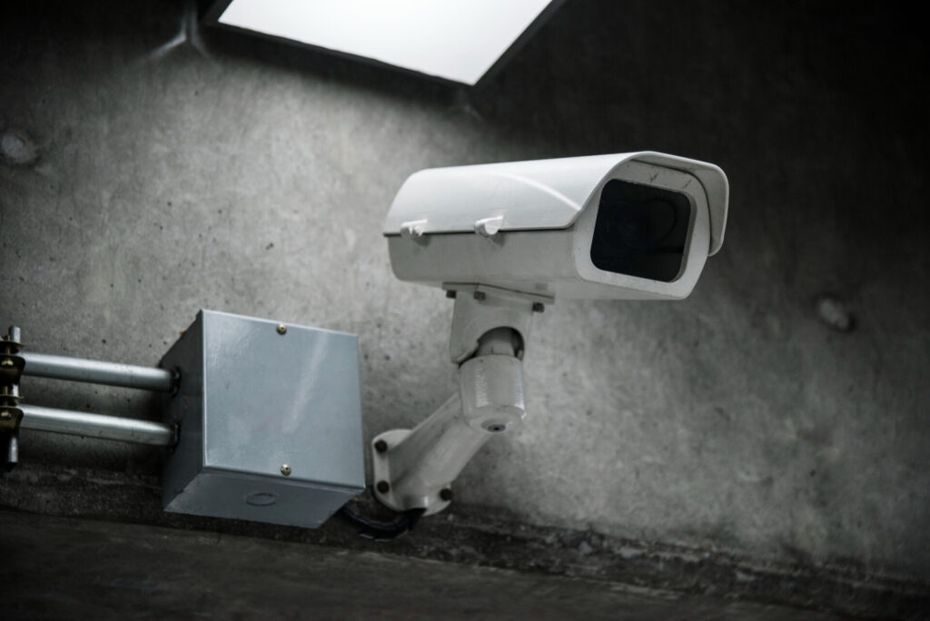 Security camera mounted on a metal arm attached to a concrete wall in an industrial space, monitoring the area.