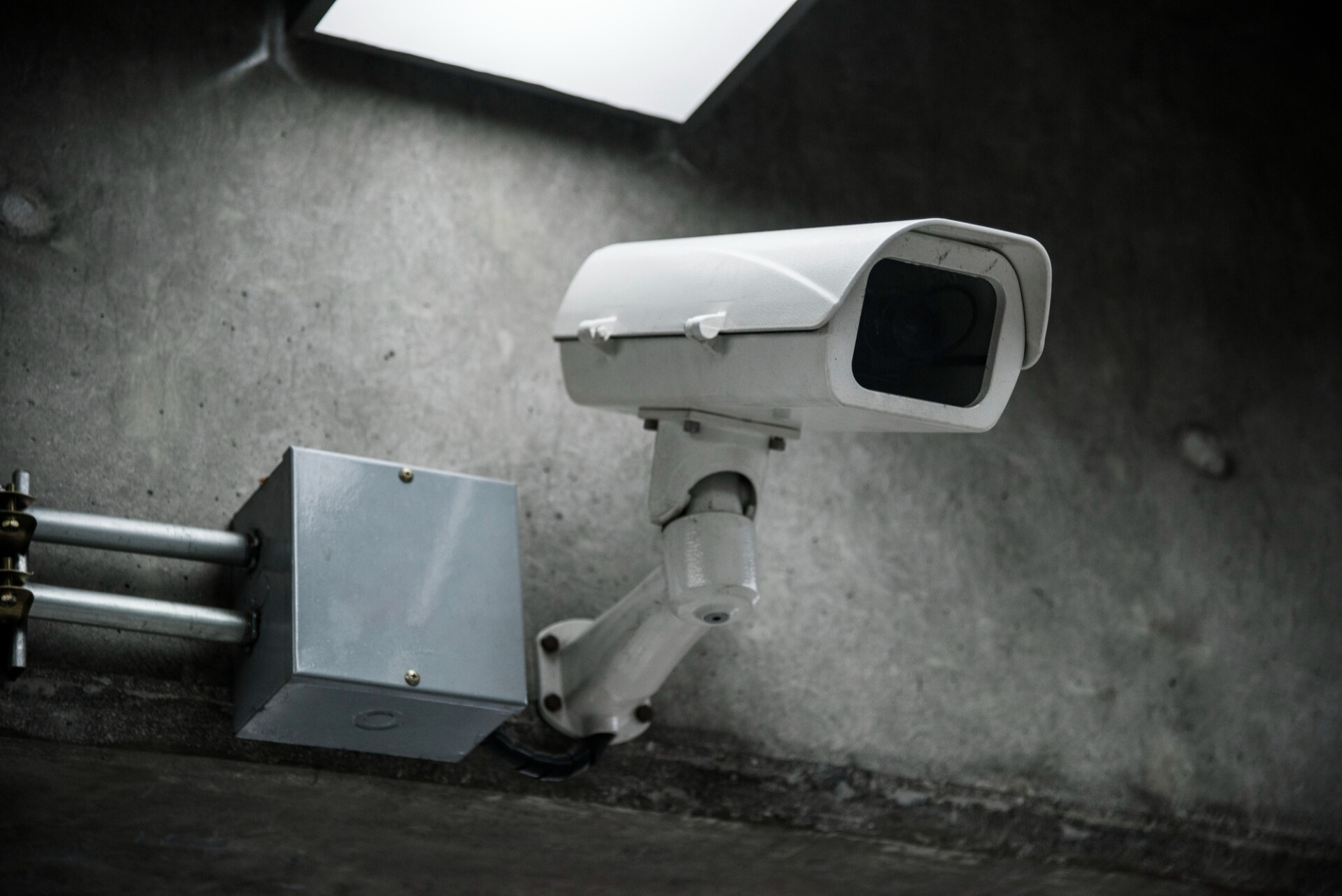Security camera mounted on a metal arm attached to a concrete wall in an industrial space, monitoring the area.