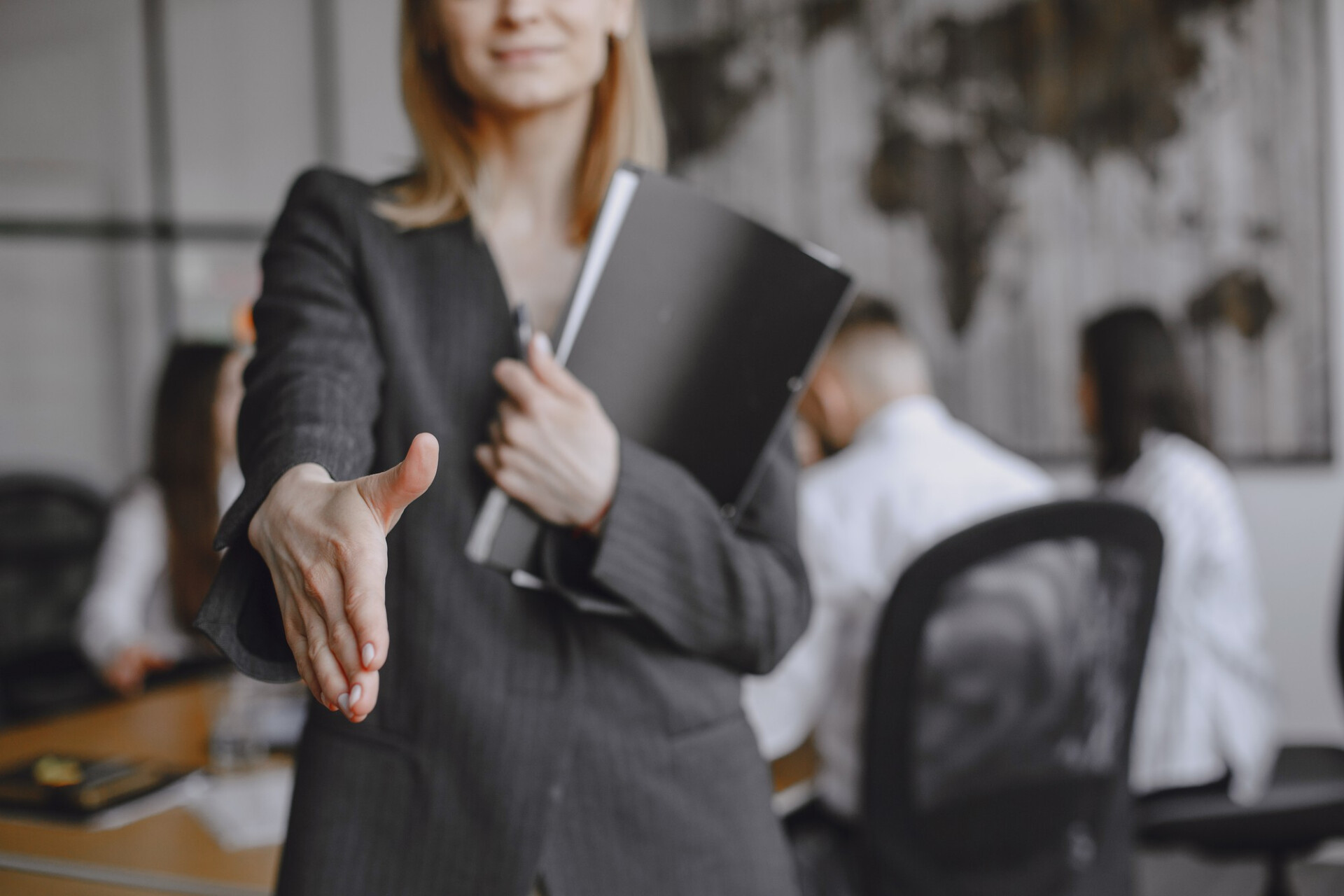 Professional woman in a dark suit extends her hand for a handshake in an office setting