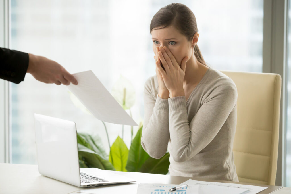 Getting Redundancy Selection Criteria Right: A Guide to Tribunal Success - Wolf Law Wolf Law 5373 Concerned woman at a desk covering her mouth while a hand hands her a document in an office setting