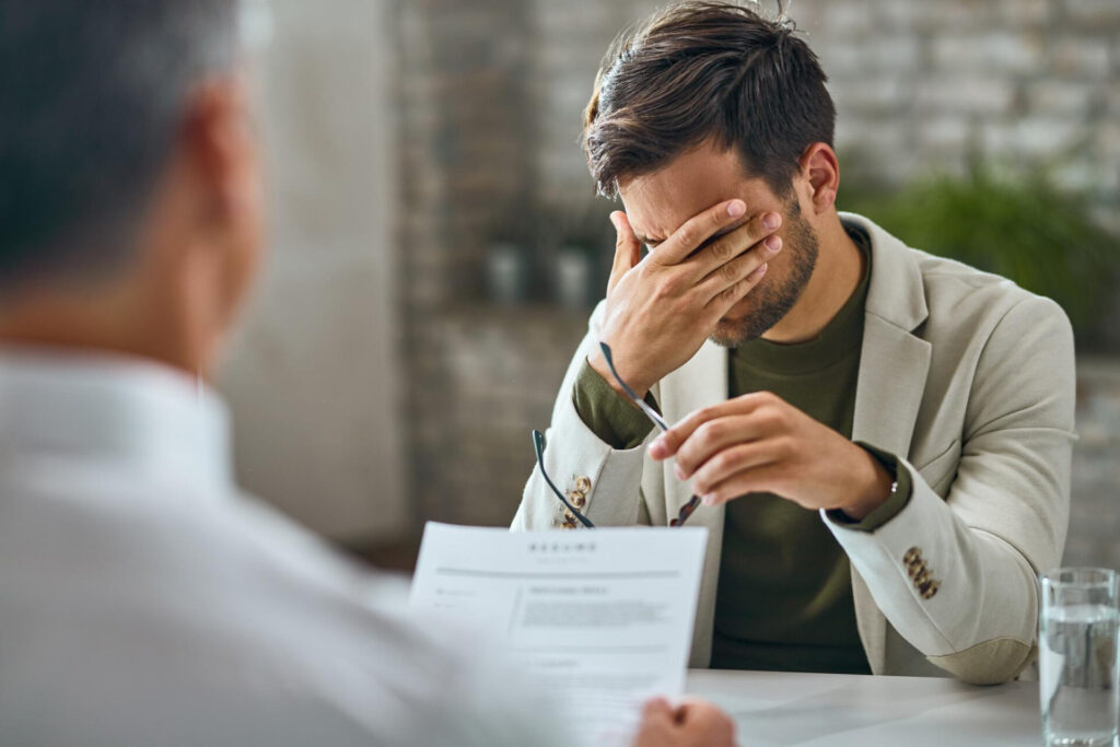 Employment Law | Expert Legal Representation | Wolf Law Wolf Law Unfair Dismissal: What Are Your Rights as an Employee? - Wolf Law Wolf Law 6553 Man in a beige blazer sits at a table, hand covering his face in apparent frustration during a meeting.