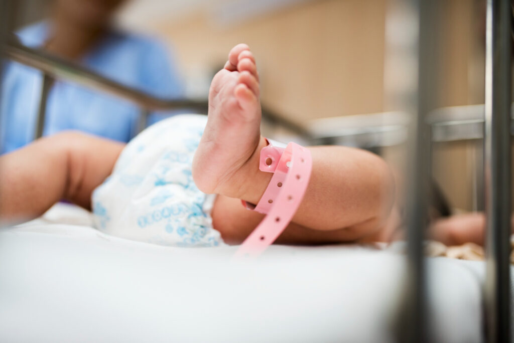 Birth Injury Medical Negligence: A Case Study in Clinical Accountability - Wolf Law Wolf Law 14344 Close-up of a baby's foot with a pink hospital ID bracelet in a crib or bassinet.