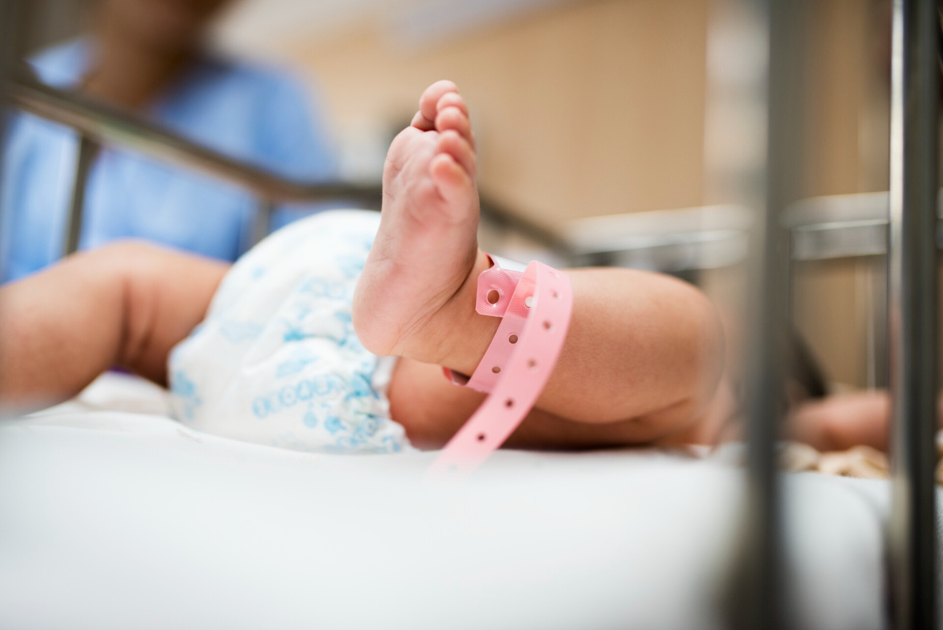 Close-up of a baby's foot with a pink hospital ID bracelet in a crib or bassinet.