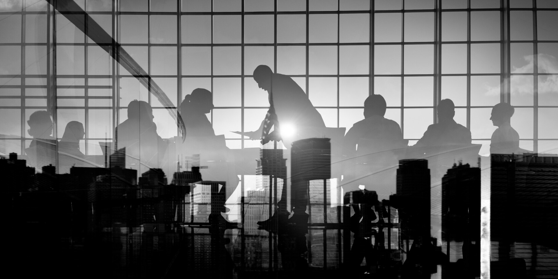 Silhouetted business meeting in a glass-walled conference room overlooking a city skyline.