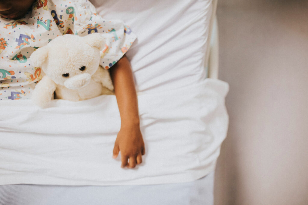 Children injured by NHS negligence can claim damages for lifetime lost earnings - Wolf Law Wolf Law 63311 Child in bed holding a white teddy bear, wearing colorful patterned pajamas.