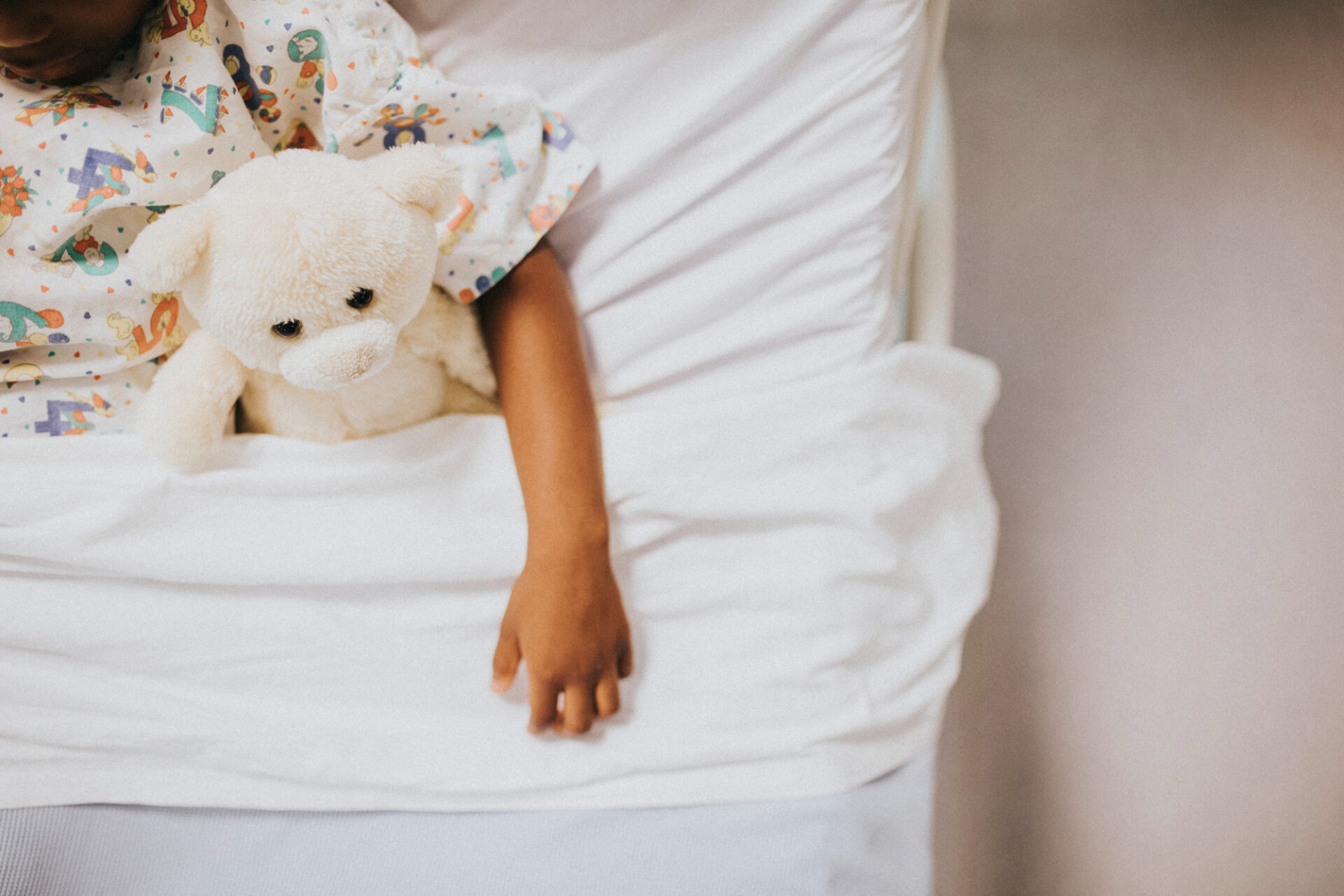 Child in bed holding a white teddy bear, wearing colorful patterned pajamas.