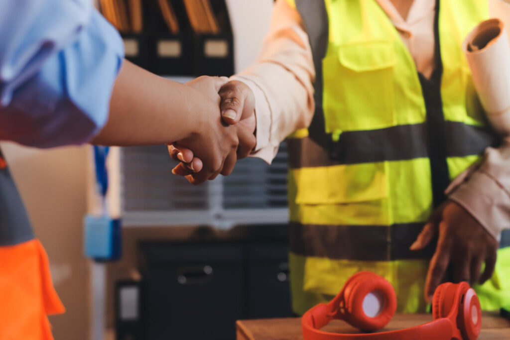 Employment Law Update: Key Changes and Protections for UK Workers in 2026 - Wolf Law Wolf Law 120984 Two people shake hands in a workshop; one wears a yellow safety vest, suggesting a collaborative moment at a construction site.