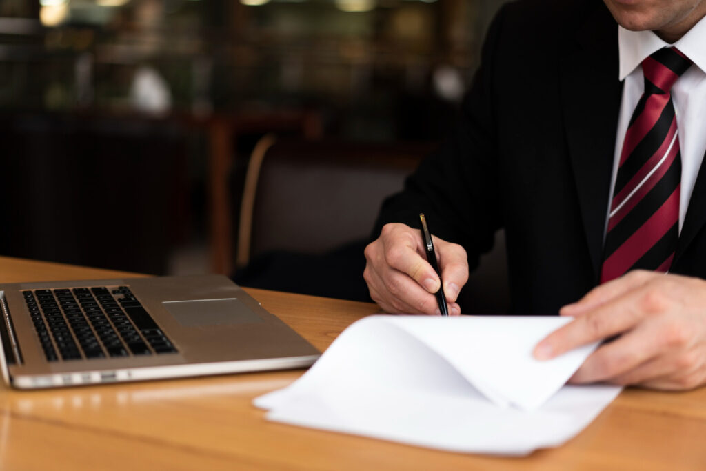 Employer Failed to Provide Work? Your Right to Compensation - Wolf Law Wolf Law 2148377785 Businessperson in a suit signs documents with a pen at a wooden desk beside an open laptop.