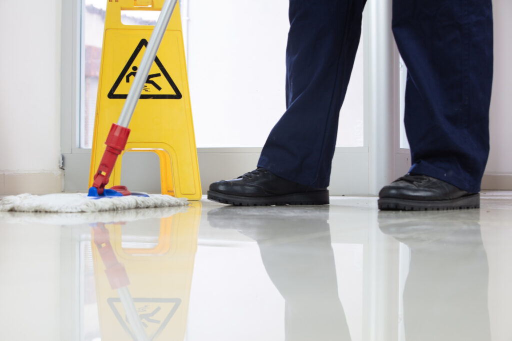 Wolf Law are the number one accident solicitors in Liverpool and the Wirral, supporting claims for personal injury claims in Liverpool Wolf Law are the number one accident solicitors in Liverpool and the Wirral, supporting claims for personal injury claims in Liverpool Caution sign beside a mop on a wet hallway floor, reflecting in the shiny surface. A person in dark pants and black shoes stands nearby.