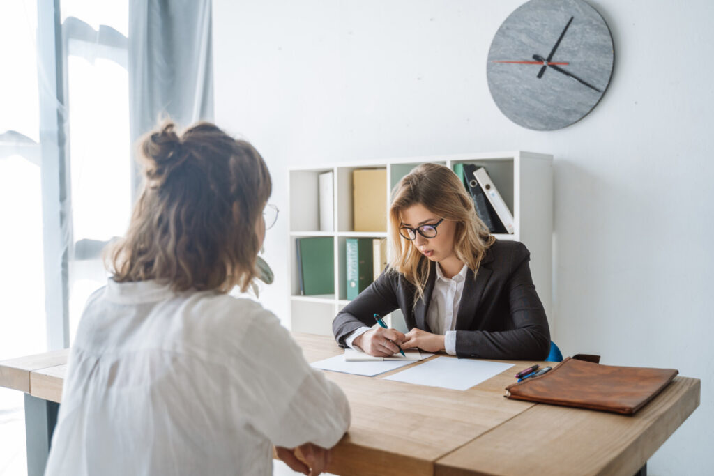 Understanding Unfair Dismissal Claims in the UK Employment Law - Wolf Law Wolf Law 3832 Two professionals sit across a wooden table in a bright office; a woman in a blazer writes notes while the other person listens.