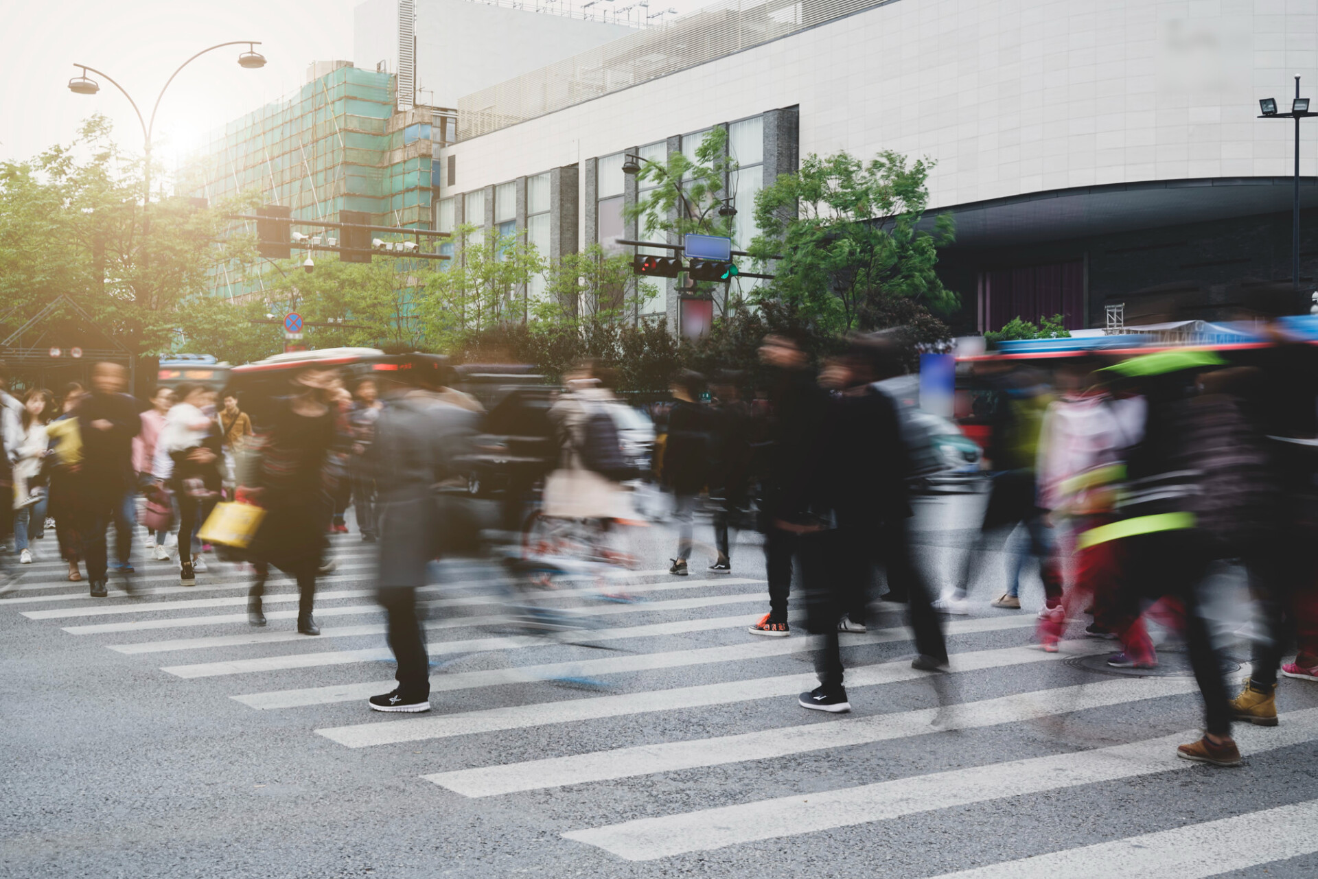 Crowded city crosswalk with pedestrians moving quickly in front of modern buildings behind them.