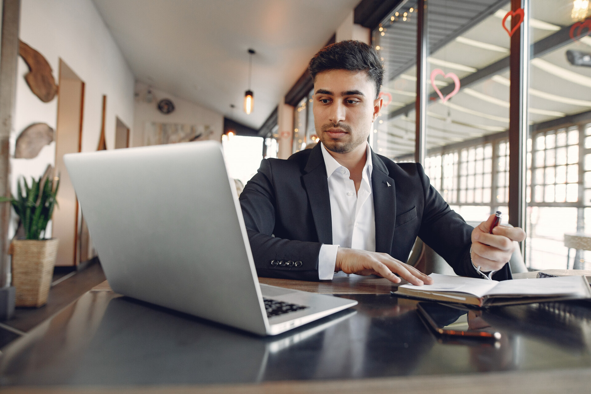 Man in a suit sits at a desk with a laptop, reviewing documents in a modern office setting.